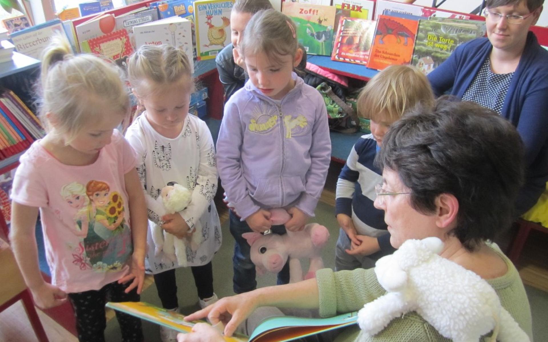 Frau zeigt Kindern, die vor ihr stehen, etwas in einem Buch