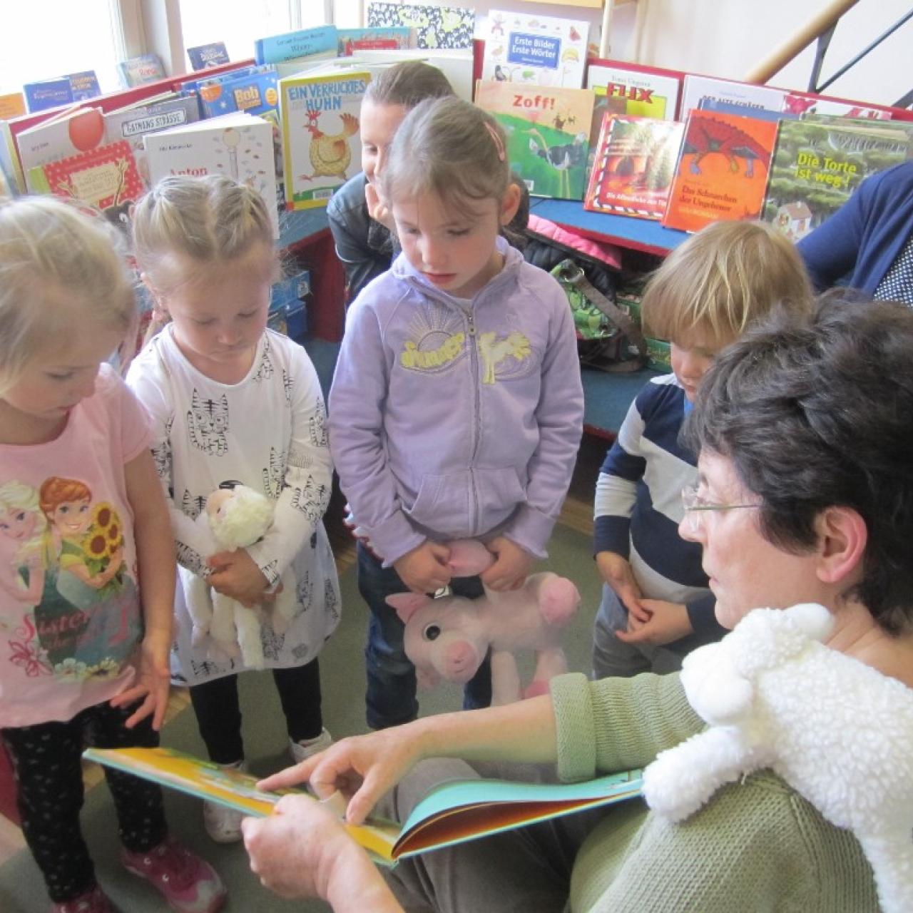 Frau zeigt Kindern, die vor ihr stehen, etwas in einem Buch